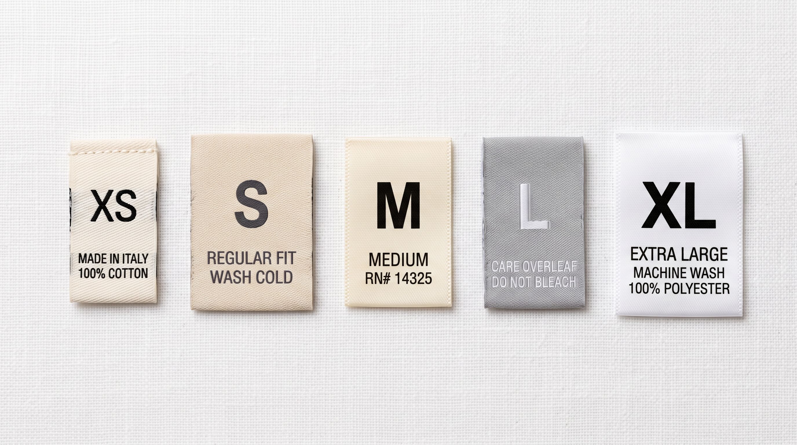 Fabric garment size labels in different format styles laid flat on white surface for comparison