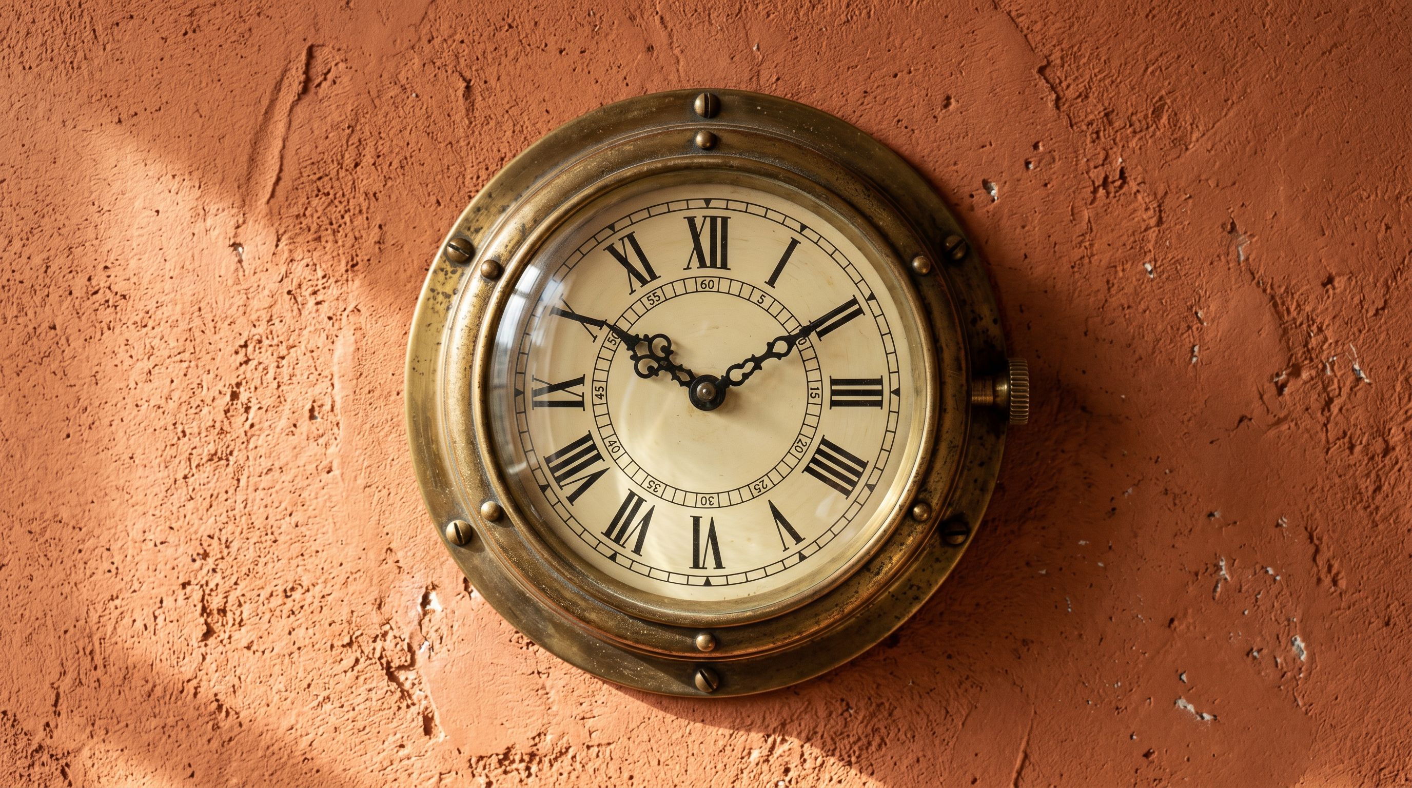 A vintage brass wall clock face mounted on a terracotta plaster wall with raking side light.