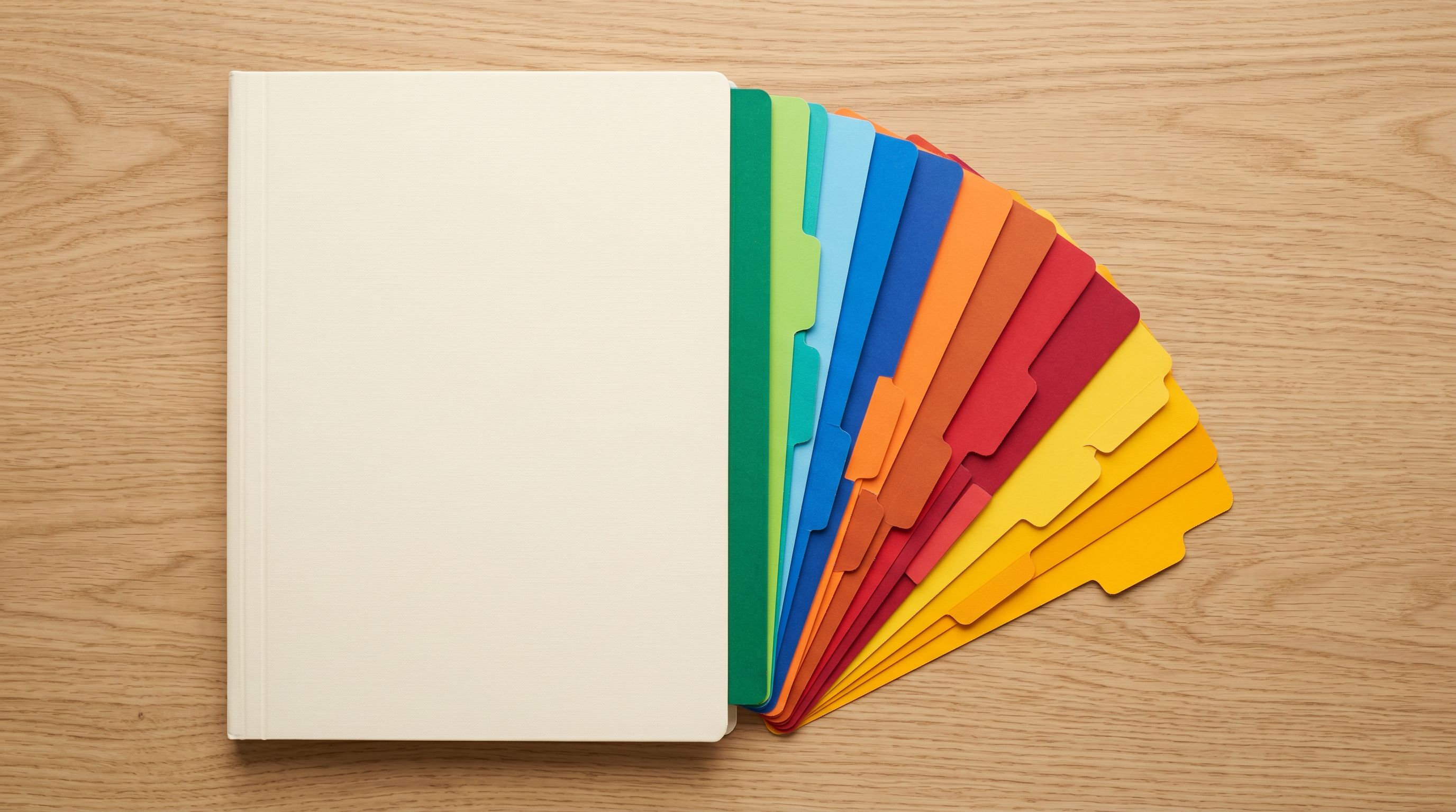 Multicoloured filing divider tabs fanning from a pale folder representing organised Shopify category and Industry Pack selection.