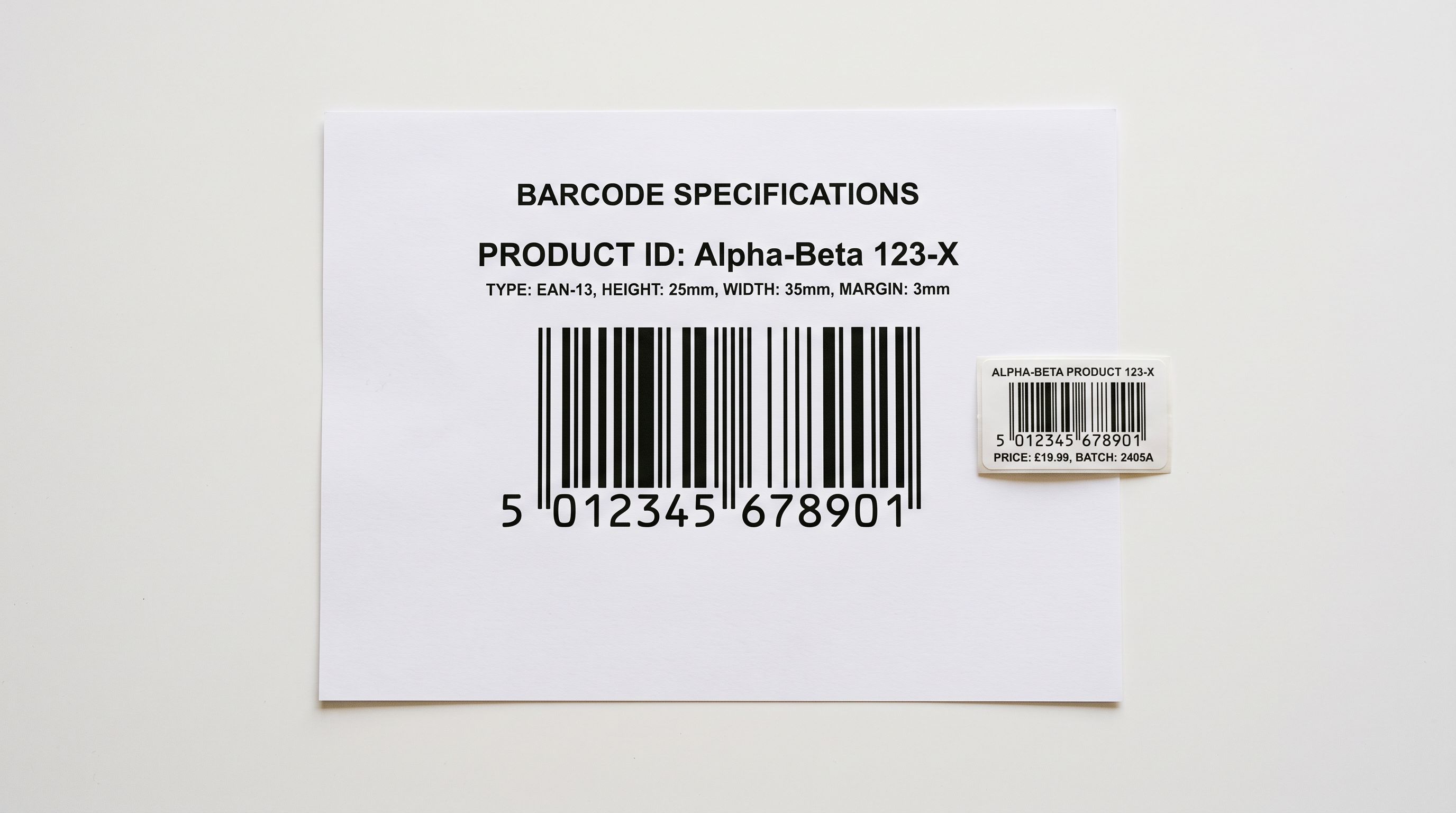 A printed barcode specification sheet resting on a white surface showing a product barcode with numerical digits and a GTIN label beside a small product tag, under even studio lighting.