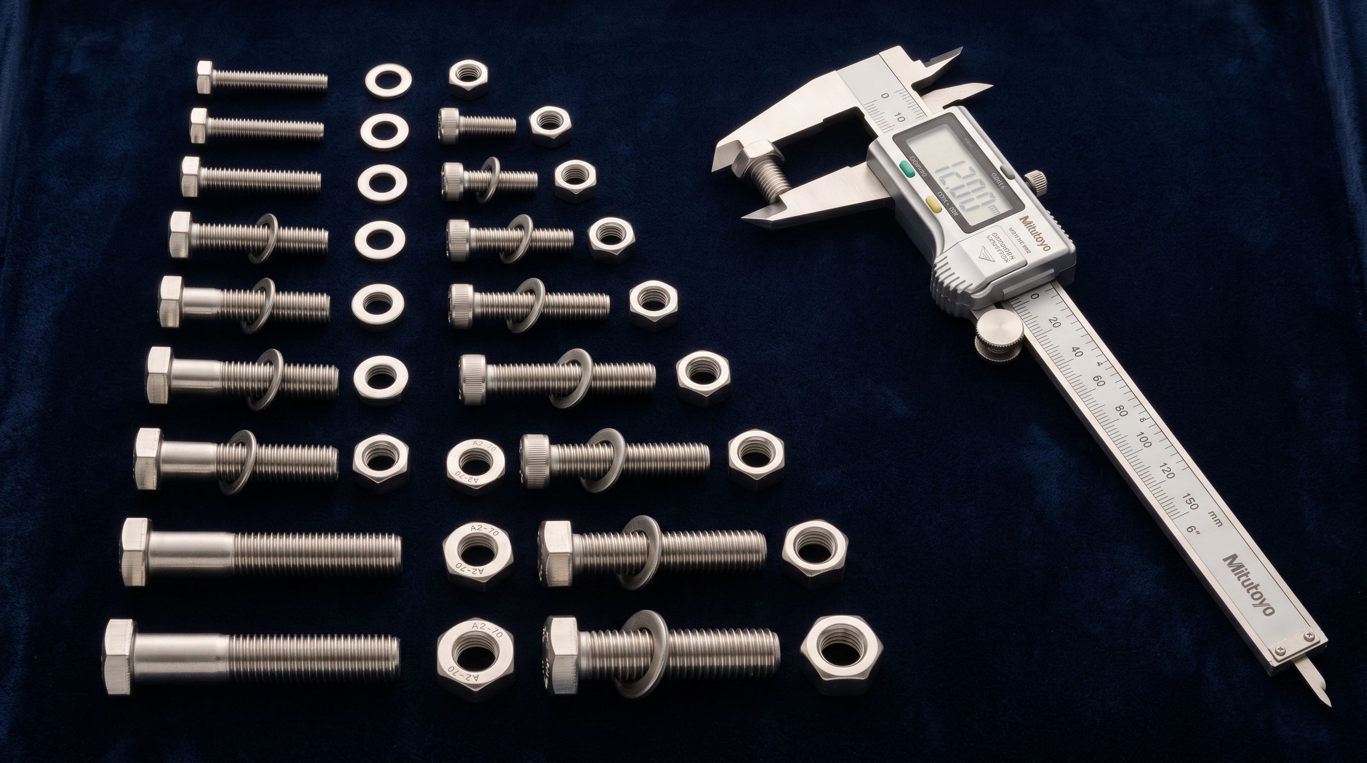 Stainless steel machine screws bolts and hex nuts arranged by diameter on dark velvet with engineer calipers beside them