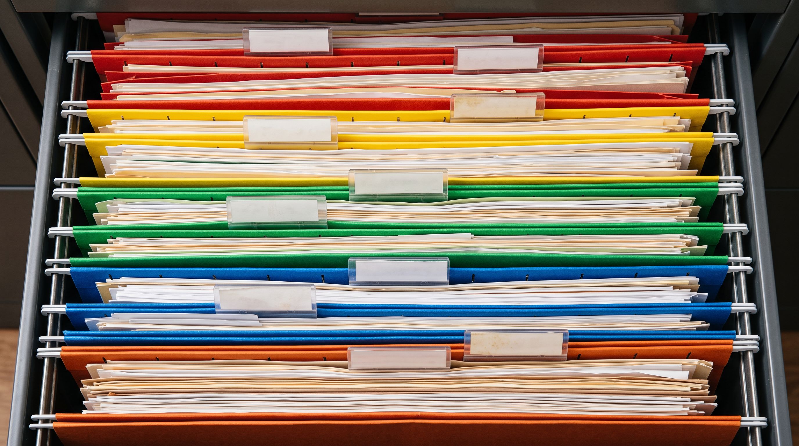Overhead view of colour-coded hanging folders in green, blue, red and yellow in an open filing drawer.