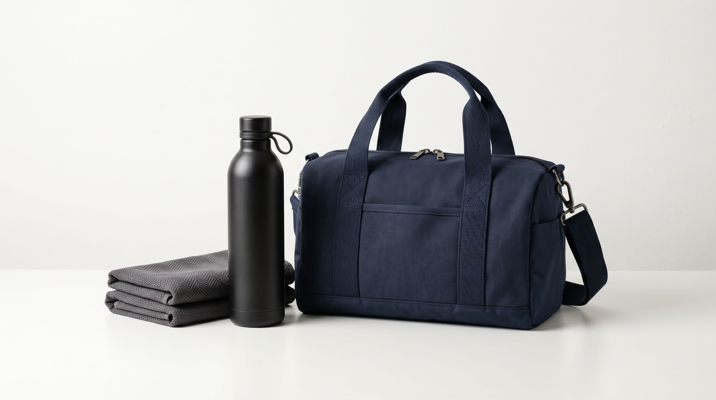 Three complementary retail products arranged as a curated gift bundle on a white surface: a stainless steel water bottle, a folded sports towel, and a compact gym bag displayed together as a curated set.