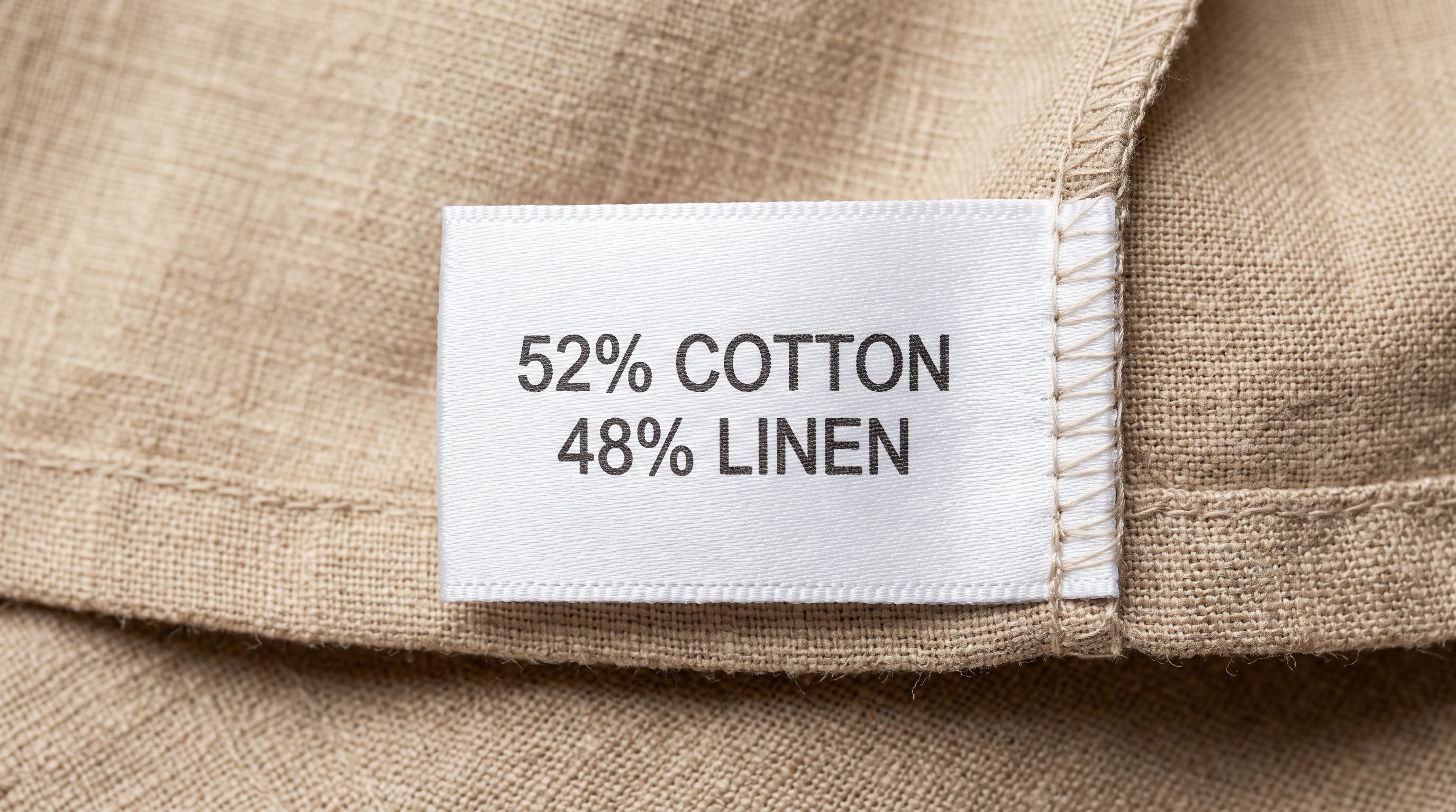 Close-up of a fabric composition label showing percentage breakdown of cotton and linen fibres on a white care instruction tag sewn into a fabric hem.