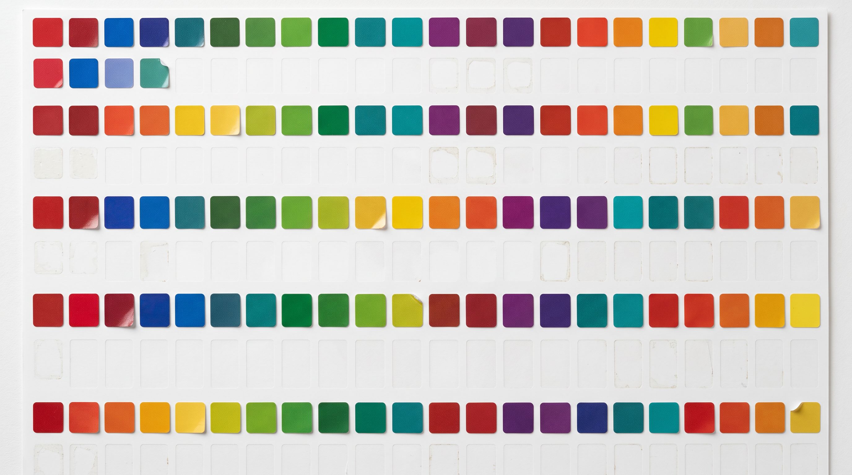 Rows of small coloured adhesive product labels arranged in a taxonomy grid on a white sorting surface with several label positions blank and empty