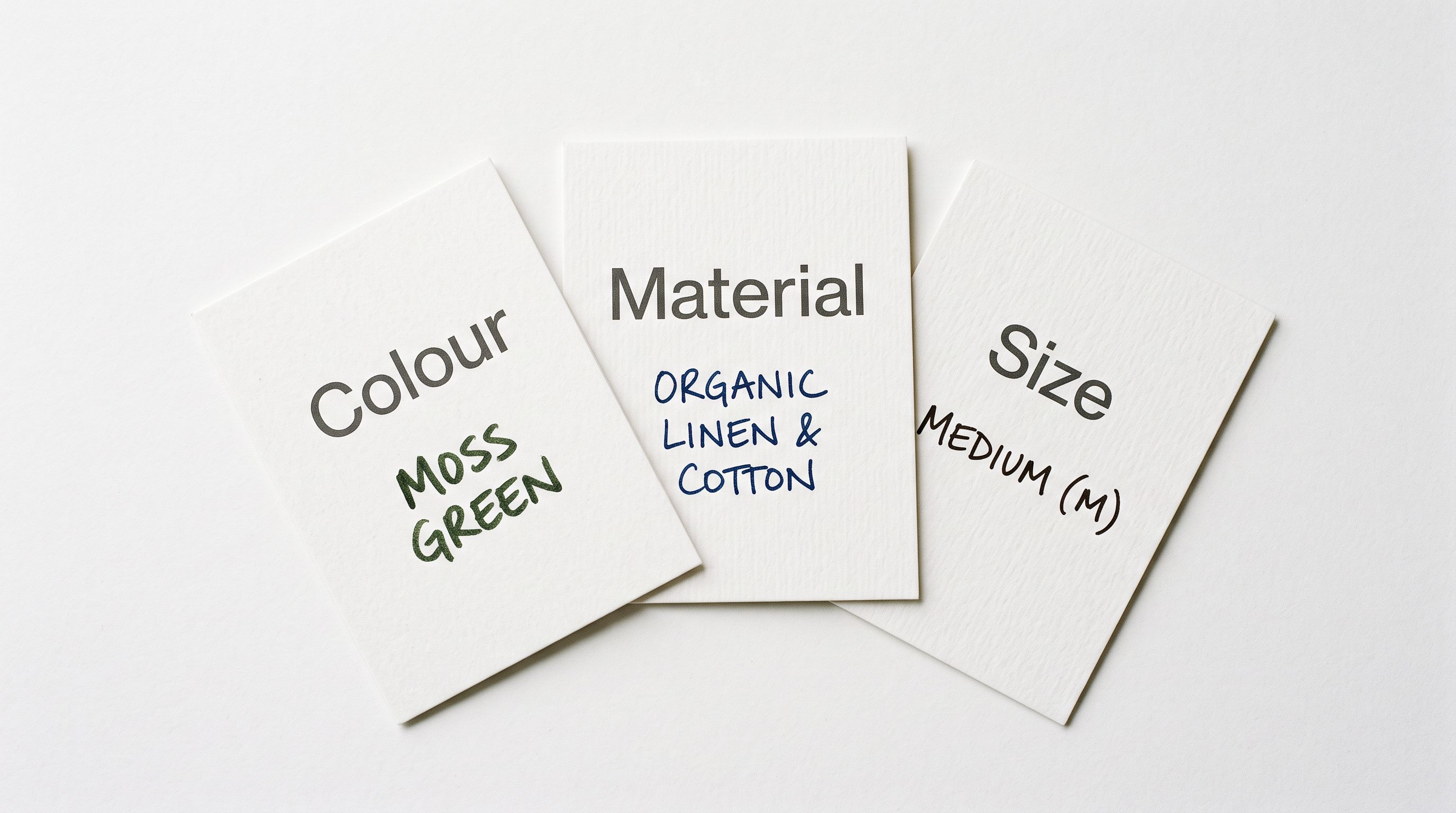 Product attribute specification cards fanned out on a white surface each card showing a single attribute name in clean type with a sample value written below representing structured product metadata