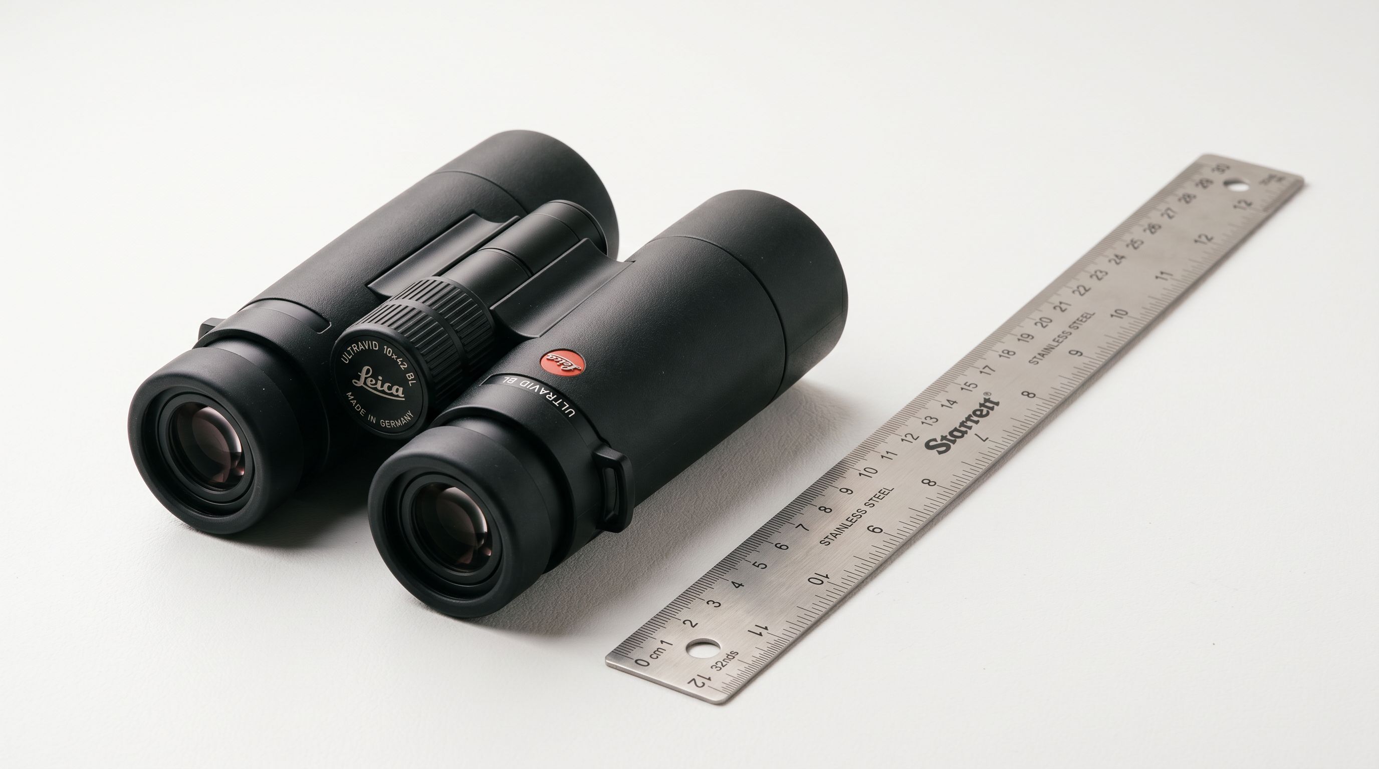 Professional binoculars and precision ruler on white surface representing product specification data.