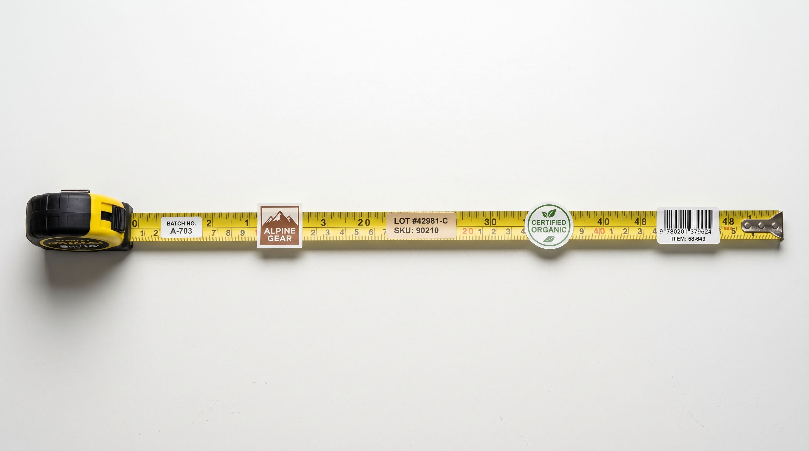 A tape measure stretched across a plain white desk with product labels placed at different lengths along it.
