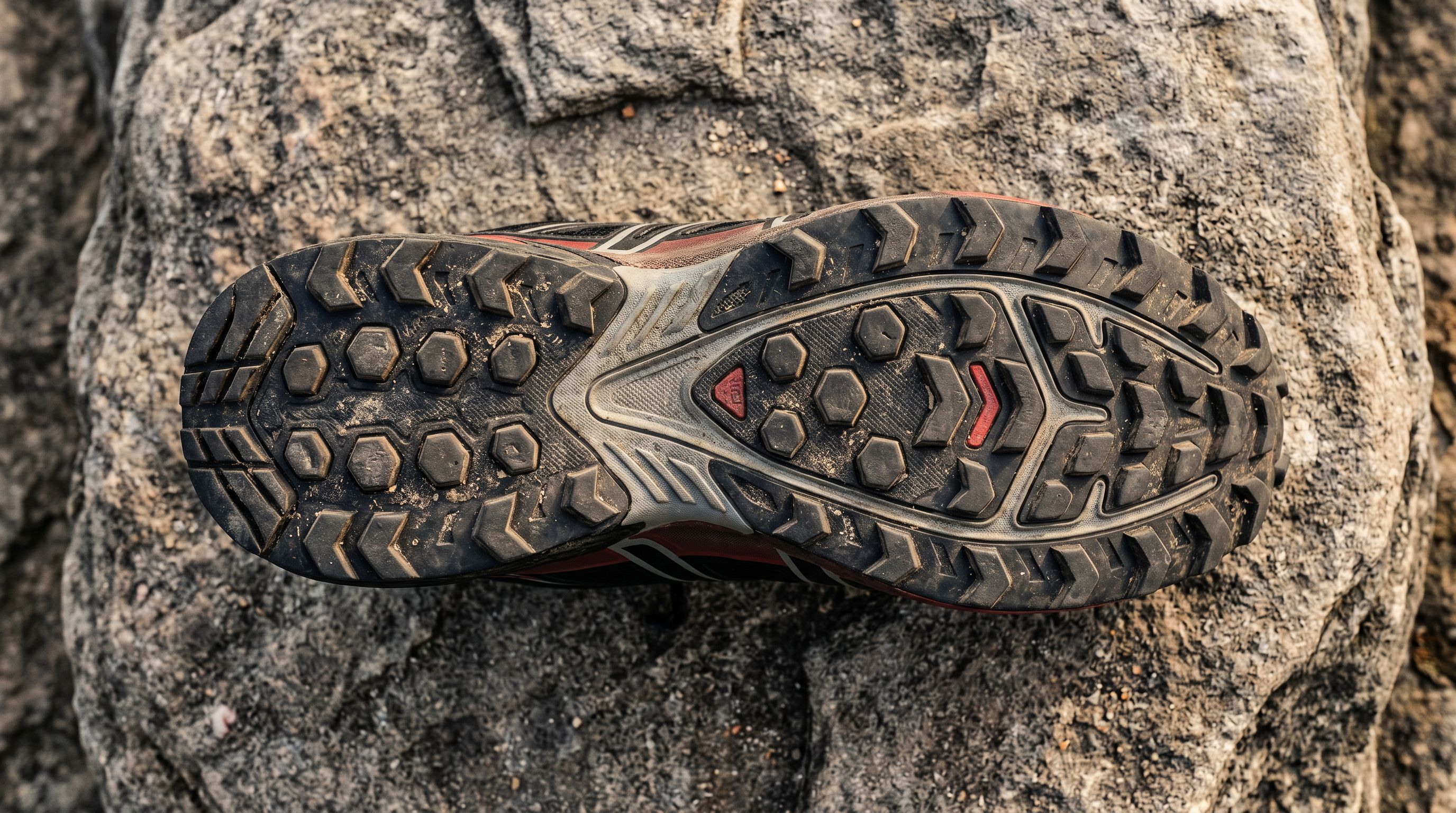 Close-up overhead view of a trail running shoe outsole on natural stone showing deep rubber lug grip pattern detail.